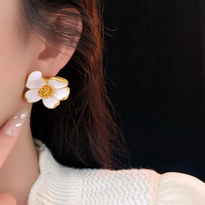 Close-up of white enamel flower earring with gold trim and center on a model