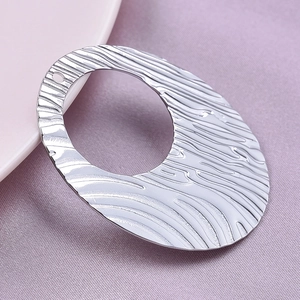 Macro view of silver oval pendant featuring wave texture and hollow design on a ceramic plate