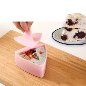 Pink triangular rice ball mold with manual press handle on a wooden cutting board