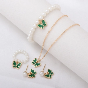 Parure bijoux papillon dorée avec émail vert et perles blanches sur tissu blanc