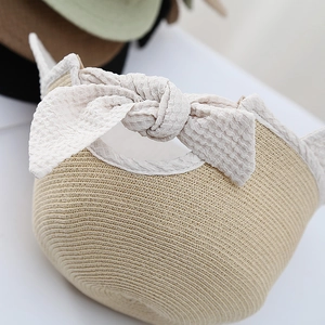 Detailed view of straw sun hat featuring a large white bubble texture ribbon bow tie