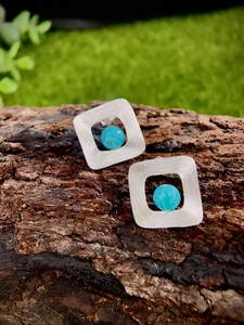 Detail of square silver earrings with turquoise beads placed on rustic tree bark