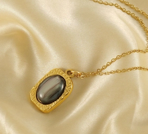 Detail of 18K gold-plated square pendant with natural stone on draped silk fabric