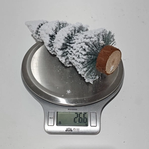 Mini cedar Christmas tree with white flocking on a scale weighing 26.6 grams