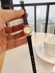 Close-up of vintage gold watch with Roman numerals on white dial and black leather strap