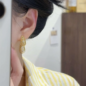 Close-up of elegant gold hollow drop earrings with diamonds worn by a model