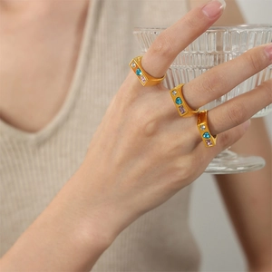 Three gold square rings with blue pink and clear gems on a hand holding glass