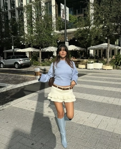 Detalle de un suéter de punto azul claro combinado con una minifalda plisada beige y botas