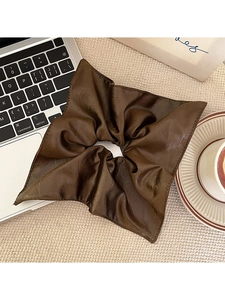 Detail shot of a large brown pleated faux leather hair tie in a lifestyle setting