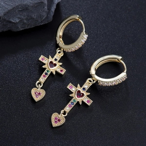 Gold cross and heart drop earrings with colorful zircon stones on a dark stone background