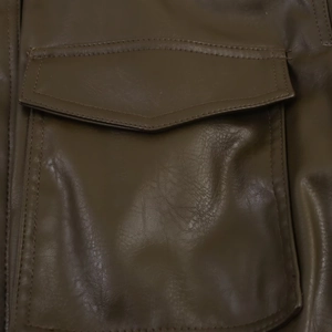 Détail d'une veste en cuir marron foncé avec rabat de poche et coutures apparentes