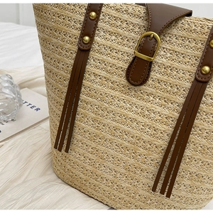 Close-up of woven straw tote bag with brown leather strap and gold metal rivets