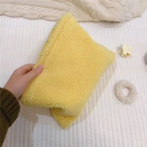 Close-up of a soft yellow faux shearling cosmetic bag held against a white quilted background