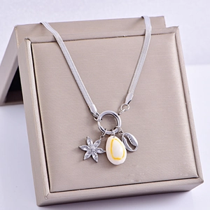 Silver snake chain necklace with shell and starfish pendants on a gold jewelry box