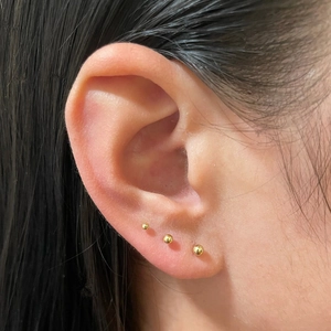 Detailed close-up of three different sizes of minimalist gold spherical stud earrings