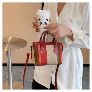 Detail of striped canvas tote with red leather handles shown in a cafe setting
