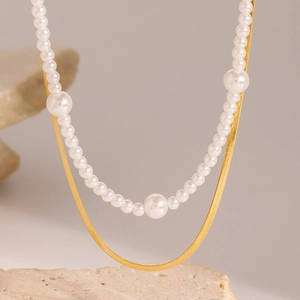 Double-layer gold snake chain and white pearl necklace on a minimalist beige stone base