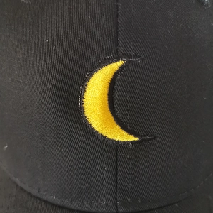 Close-up of yellow crescent moon embroidery on black cotton twill baseball cap