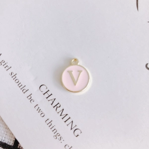 Close-up of a pink enamel round charm featuring a golden letter V for DIY jewelry making