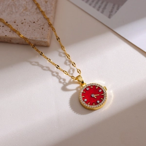 Elegant gold necklace with red watch-style pendant and crystal accents on white stone background