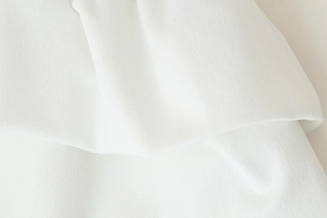 Détail macro du tissu en maille côtelée blanche avec ourlet volanté et texture douce