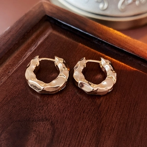 Close-up of gold-plated textured hoop earrings with irregular wave design on wood