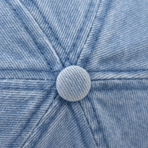 Détail du bouton supérieur et des coutures sur la casquette de baseball en denim bleu