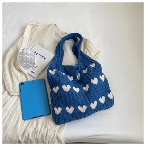 Detailed knit of blue crochet shoulder bag with white heart patterns and cable texture