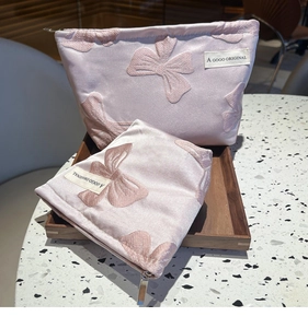 Detail of two pink satin makeup bags with 3D bow patterns and brand logo label