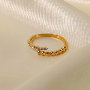 Vista macro di un anello placcato oro con cristalli e perle dorate su seta beige