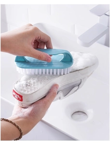 Blue plastic scrubbing brush with white bristles cleaning a canvas sneaker sole with soap