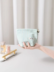 Striped fabric cosmetic bag with floral charm and blue vertical stripes held by a hand