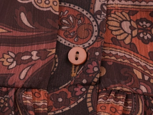 Detail shot of vintage paisley print fabric with a brown button on a long vacation dress