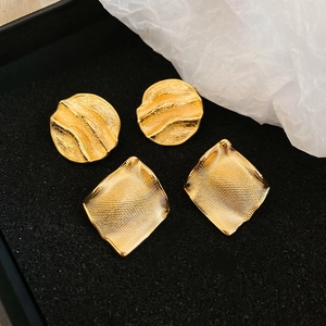 Gros plan de boucles d'oreilles dorées aux textures ondulées et maillées sur velours noir