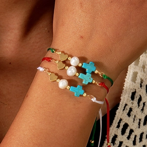 Three-piece woven bracelet set with cross, heart charms and pearls on model wrist