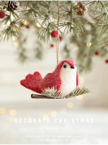 Close-up of handmade red and white felt bird ornament hanging on a festive pine branch