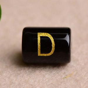 Macro detail of a black cylindrical bead featuring a gold-stamped letter D for DIY jewelry