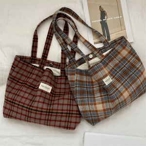 Detail of plaid wool tote bags in red-brown and blue-grey with a white logo patch