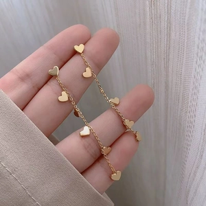 Elegant gold heart long tassel earrings in titanium steel held by hand against a fabric