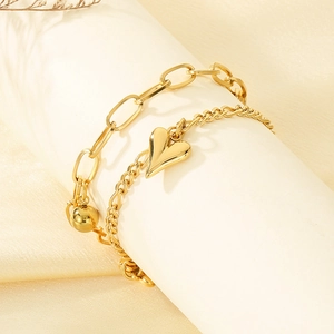 Detail eines zweischichtigen Gold-Edelstahl-Armbands mit Herzanhänger und Büroklammerkette