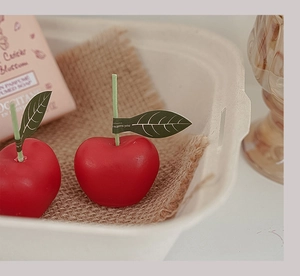 Primer plano detallado de una vela aromática con forma de cereza roja y hoja decorativa