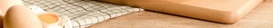 Close-up of wooden handle and fresh eggs on a plaid cloth next to the stone frying pan