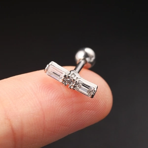 Macro view of a silver zircon ear stud with rectangular stones held on a fingertip