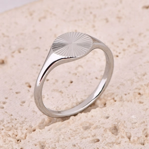 Detailed view of silver sunburst signet ring on textured stone surface background