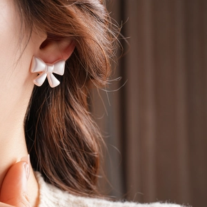 Close-up of soft pink acrylic bow earring with pearl finish worn on the ear