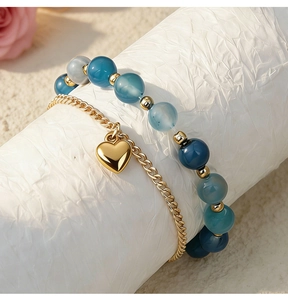 Detail of couple bracelet set with blue beads and a gold heart charm on a white stand