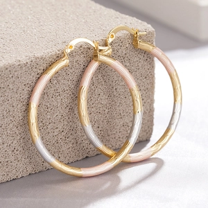 Macro shot of tri-color gold hoop earrings with polished wave pattern and snap closure