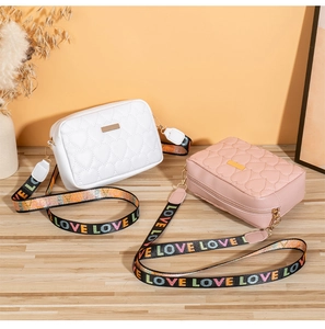 Detail of heart-quilted crossbody bags in white and pink with 'LOVE' printed strap
