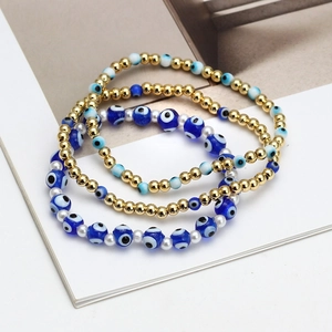 Three-piece stackable evil eye bead bracelets with gold accents and blue resin charms