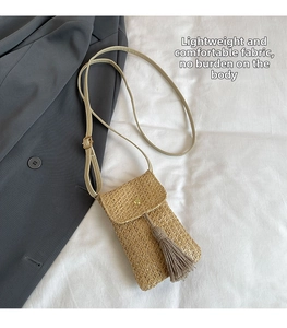 Straw woven crossbody bag with tassel detail on white fabric next to a gray blazer
